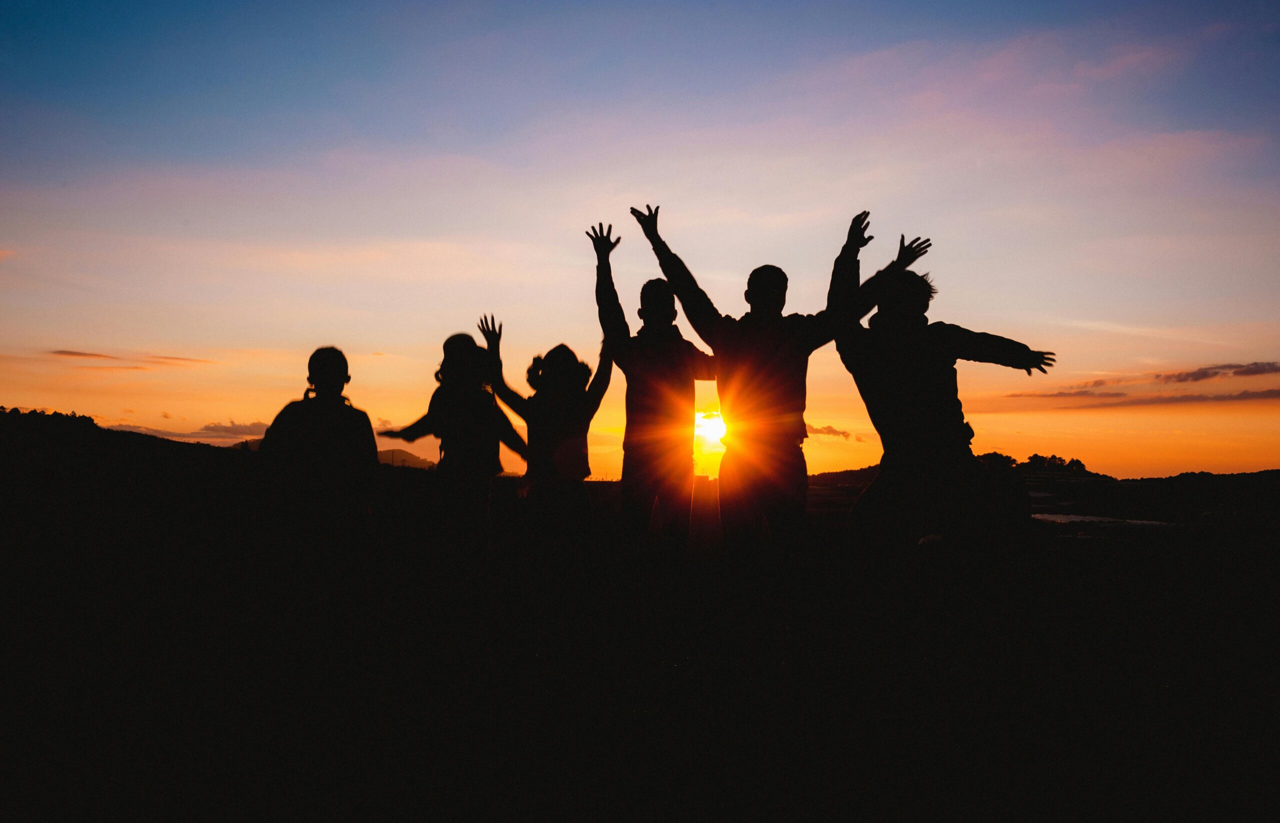 Group of friends silhouetted against a vibrant sunset sky, celebrating together outdoors.
